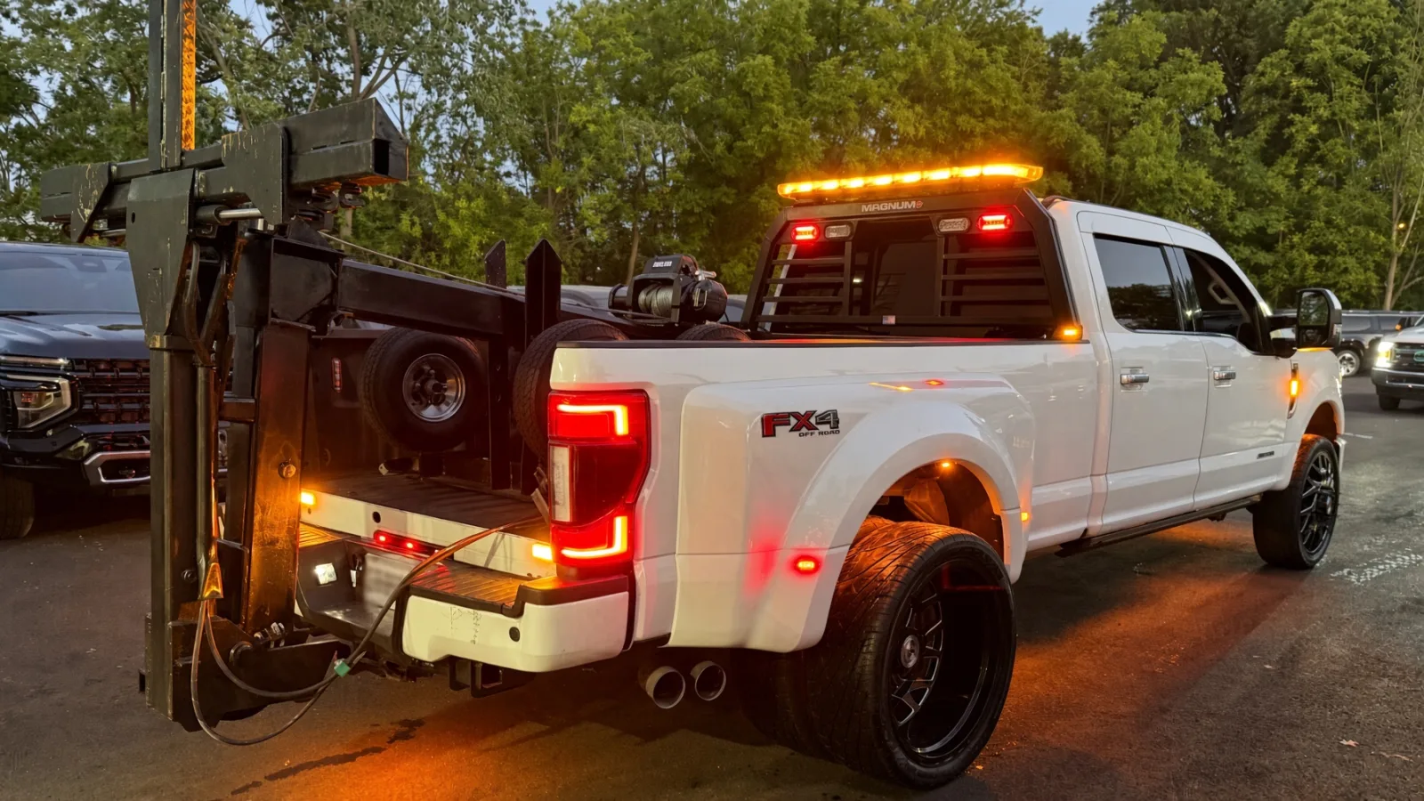 White Ford F-350 dually wrecker upfitted by Auto Action Technologies with an amber Magnum light bar, headache-rack strobes and side marker lights lit at dusk